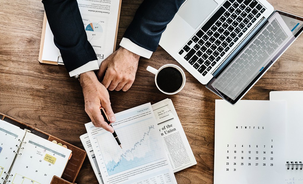 A desk with financial charts, a laptop and a cup of coffee