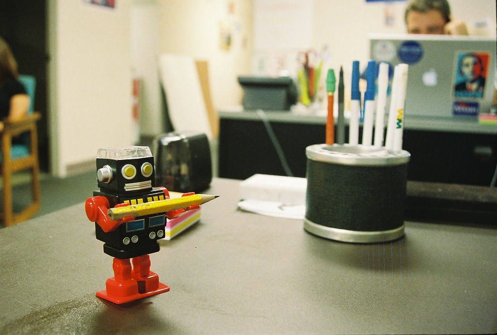 A small toy robot holding a pencil on an office desk
