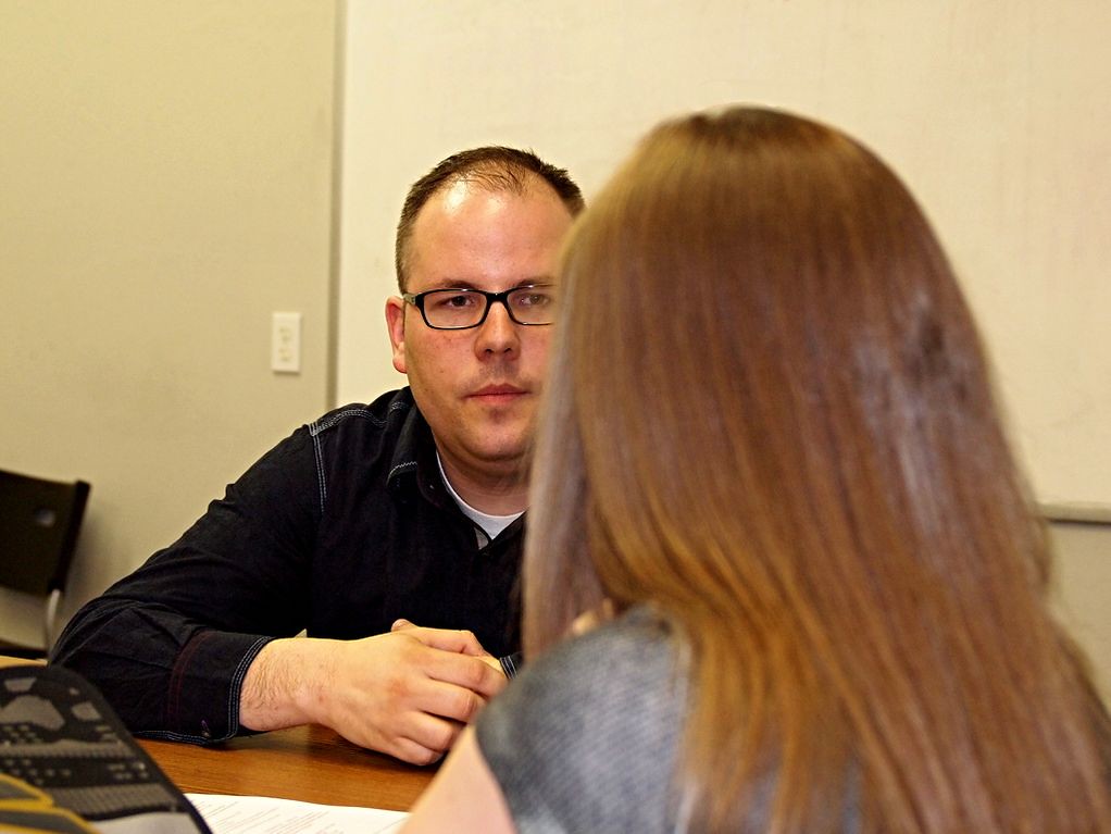Two people talking across a table, one taking notes