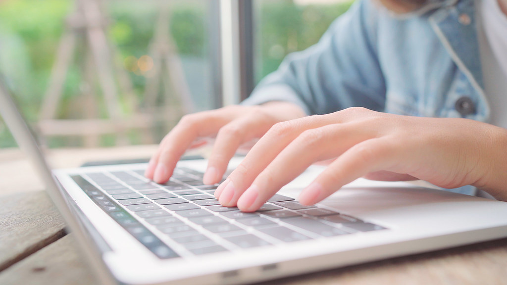 Close-up of hands typing on a laptop by a sunlit window